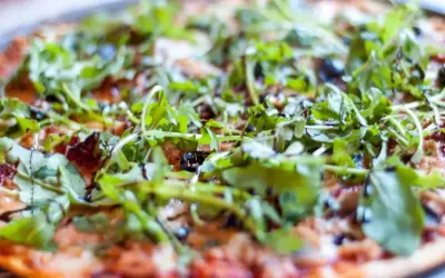 Pyszna pizza z tuńczykiem, rukolą i oliwkami, polana sosem balsamicznym.