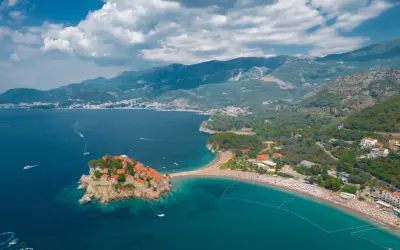 Sveti Stefan, Czarnogóra na co uważać? Urokliwa wyspa z czerwonymi dachami, połączona z lądem piaszczystą mierzeją, otoczona turkusowym morzem i zielonymi wzgórzami.