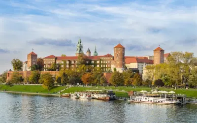 Zabytkowe miasto nad Wisłą, Wawel w jesiennej odsłonie, z łodziami cumującymi przy brzegu.