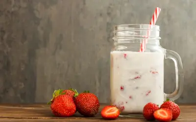 Kefir z truskawkami w słoiku z uchem, obok świeże truskawki na drewnianym stole.