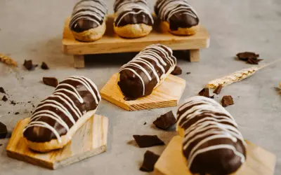 Éclairs gourmands avec un glaçage éclair chocolat brillant, décorés de fines rayures blanches. Des éclats de chocolat parsèment la table.
