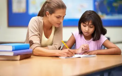 Nauczycielka pomaga uczennicy w pisaniu, wspierając ją w procesie edukacyjnym, który może być częścią orzeczenia z poradni psychologiczno-pedagogicznej.
