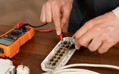 Ręce majsterkowicza mierzą rezystancję elektryczną za pomocą multimetru, badając gniazdo przedłużacza.
