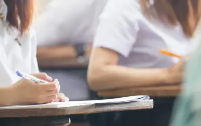 Dłoń studenta pisząca długopisem na kartce papieru podczas egzaminu.