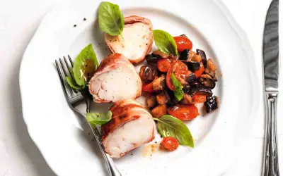 Tranci di rana pescatrice avvolti nel prosciutto, serviti con ratatouille di verdure e basilico fresco.