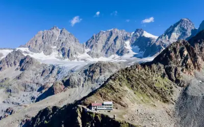 Il rifugio Marinelli, un edificio bianco e rosso, si erge su una cresta rocciosa con imponenti montagne innevate sullo sfondo.