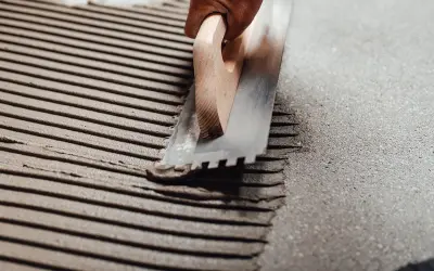 Application d'enduit pour carrelage collé avec une truelle crantée. Les sillons réguliers préparent la surface pour une pose parfaite.