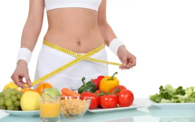 Kobieta mierzy talię centymetrem. Obok zdrowe jedzenie: owoce, warzywa, płatki. Dieta 1500 kcal efekty w zasięgu ręki!