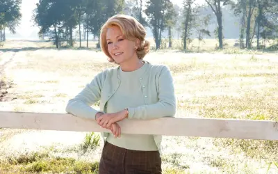 Diane Lane w pastelowym sweterku opiera się o płotek, przypominając scenę z jednego z jej filmów.