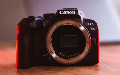 Canon EOS R10 w teście. Ciemna obudowa aparatu z czerwonym podświetleniem, widoczny bagnet obiektywu.