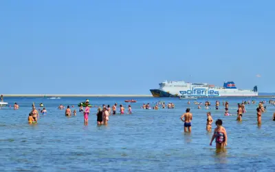 Ludzie kąpią się w morzu, a w tle płynie prom do Ystad.