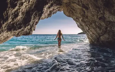 Kobieta wchodzi do turkusowej wody z jaskini. Idealne miejsce na wakacje all inclusive w Albanii.