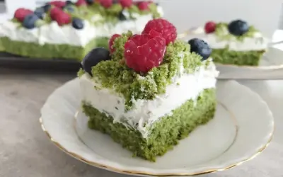 Zielony tort z bitą śmietaną i owocami leśnymi, przypominający leśny mech.