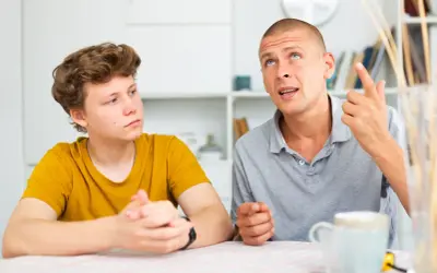 Ojciec tłumaczy synowi, jak rozmawiać z nastolatkiem, używając gestów. Chłopiec słucha uważnie.