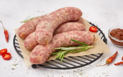 Surowa biała kiełbasa na ruszcie, gotowa do przygotowania. Obok papryczki chili i sos. Idealna do gotowania.
