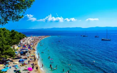 Wyspa Brać oferuje niezapomniane atrakcje: plaża Zlatni Rat tętni życiem, ludzie kąpią się w turkusowej wodzie, a żaglówki kołyszą się na morzu.