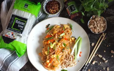 Pyszny pad thai z wołowiną, makaronem ryżowym i orzeszkami ziemnymi. Obok składniki: makaron, sos i płatki chili.
