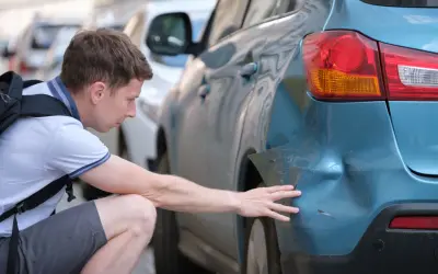 Mann untersucht Delle am blauen Auto. Hoffentlich keine Geisterfahrer-Strafe wegen des Schadens.