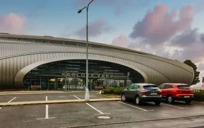 Nowoczesne lotnisko w Czechach, Karlowe Wary, z charakterystyczną, falistą fasadą. Dwa samochody stoją na parkingu przed wejściem.