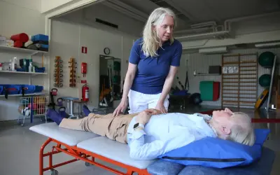 Fysioterapeut undersöker en patient som ligger på en brits. Patienten verkar vara fixerad bebis i sin position, redo för behandling.