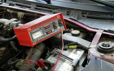 Czerwony prostownik podłączony do akumulatora w samochodzie. Wskazówki dotyczące tego, jak odłączyć prostownik od akumulatora, są kluczowe dla bezpieczeństwa.