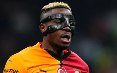 Piłkarz Osimhen w masce ochronnej na twarzy, w pomarańczowo-czerwonej koszulce z herbem Galatasaray.