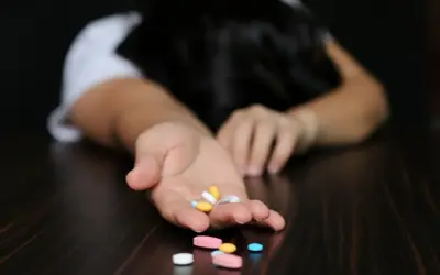 Dłoń z garścią tabletek, w tym alprazolam, na ciemnym blacie.