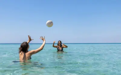 Dos amigas juegan voleibol en el mar turquesa de la playa América, bajo un cielo azul despejado.