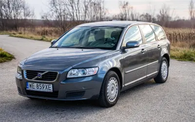 Szary Volvo V50 2.0D na drodze, z drzewami w tle.