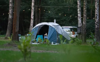 Namiot i samochód w lesie, idealne miejsce na ferie 2026 śląskie. Girlanda świetlna dodaje uroku.