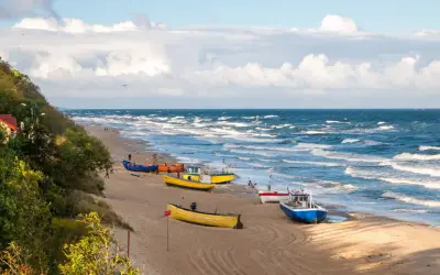 Kolorowe łodzie rybackie na piaszczystej plaży, falujące morze i zielone wzgórze tworzą malowniczy widok polskiego morza.