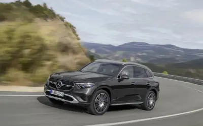 Czarny Mercedes GLC 200 4MATIC pokonuje zakręt na górskiej drodze, otoczony zielonymi wzgórzami i skalistymi zboczami.
