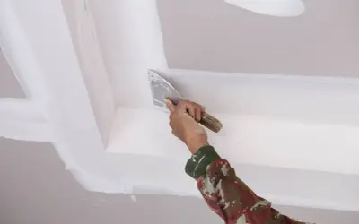 Mano aplicando masilla para techo escayola con espátula, alisando juntas y esquinas para un acabado perfecto.
