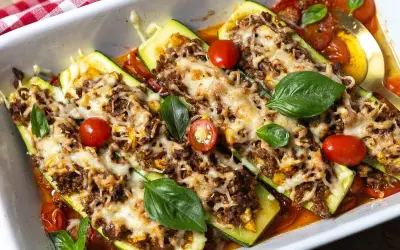 Herzhafte zucchini schiffchen mit Hackfleisch und Käse überbacken, garniert mit frischem Basilikum und Kirschtomaten.