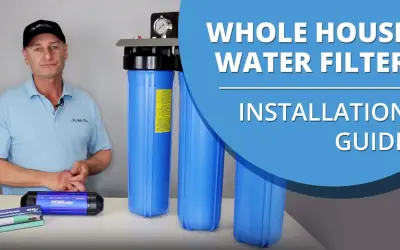 Man in a cap and polo shirt stands next to a whole house water filter system, ready for installation.
