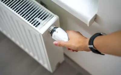 Dłoń reguluje termostat grzejnika. Zastanawiasz się, dlaczego grzejnik jest zimny na dole? Może to być problem z odpowietrzeniem lub cyrkulacją wody.