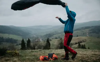 Osoba w niebieskiej kurtce i czerwonych spodniach rozkłada śpiwór puchowy czy syntetyczny na tle górskiego krajobrazu.