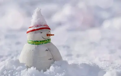 Mały bałwanek w czapce i szaliku, otoczony śniegiem. Czeka, aż spadnie więcej śniegu, by mógł się bawić.