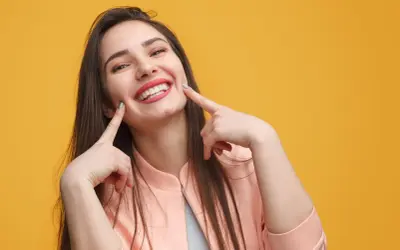 Une jeune femme au sourire éclatant, doigts pointés vers ses joues, semble expliquer la signification d'un sourire pincé.