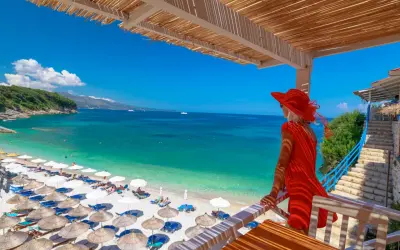 Kobieta w czerwonej sukience podziwia turkusowe morze i plażę z leżakami. Idealne miejsce na tanie kraje na wakacje.