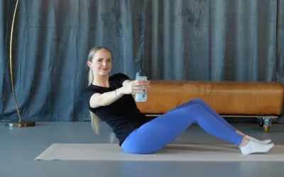 Frau macht isometrisches Krafttraining mit einer Wasserflasche. Sie sitzt auf einer Matte und dreht ihren Oberkörper.