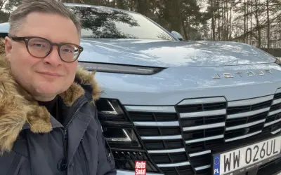 Mężczyzna w okularach i futrzanej kurtce pozuje do selfie przed jasnoniebieskim Jetour Dashing na tle zimowego lasu.