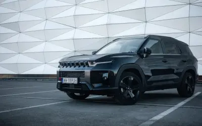 Czarny SsangYong Torres z czarnymi felgami stoi na parkingu przed nowoczesnym budynkiem o geometrycznej fasadzie.