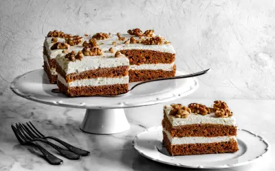 Pyszne ciasto marchewkowe z mascarpone, udekorowane orzechami włoskimi, prezentuje się apetycznie na białej paterze.