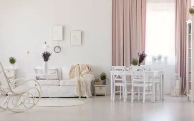 Jasny salon w stylu prowansalskim. Biała kanapa, fotel bujany, stół z krzesłami i lawenda tworzą przytulną atmosferę.