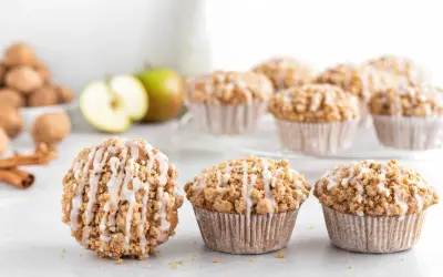 Leckere Apfelmuffins mit Streuseln und Zuckerguss, perfekt für ein Apfelmuffins Rezept. Daneben liegen Äpfel und Zimtstangen.