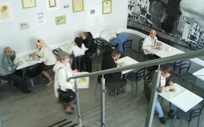 Wnętrze baru turysta. Ludzie jedzą przy stolikach, jeden z nich niesie tacę z jedzeniem.