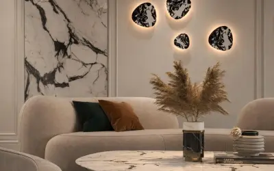Nowoczesny salon z beżową sofą i marmurowym stolikiem. Na ścianie wiszą dekoracyjne kinkiety z kloszem, tworząc ciepłą atmosferę.