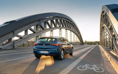 Granatowy Opel Astra jedzie przez most. Zbliża się opel akcja serwisowa, warto sprawdzić stan techniczny auta.