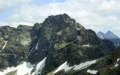 Majestatyczny kozi wierch w Tatrach, z resztkami śniegu na zboczach, pod błękitnym niebem z chmurami.